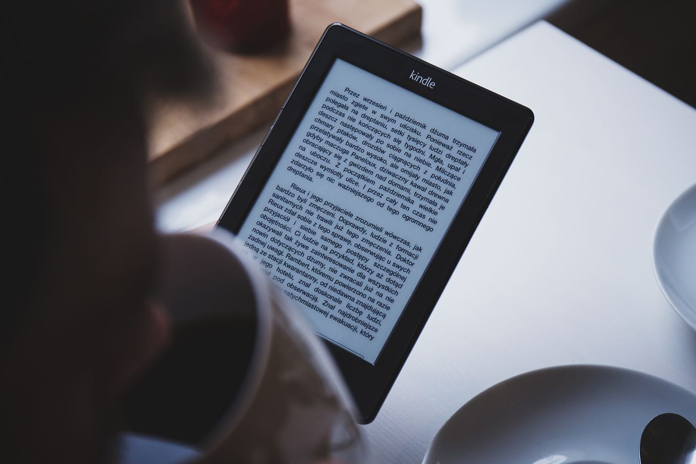 Person reading an e-reader beside a cup